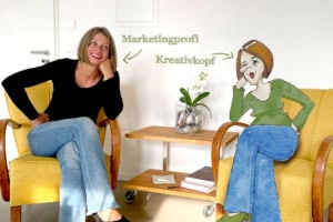Monika Moche sitzt im Sessel und klatsch ihre gezeichnete Figur ag.