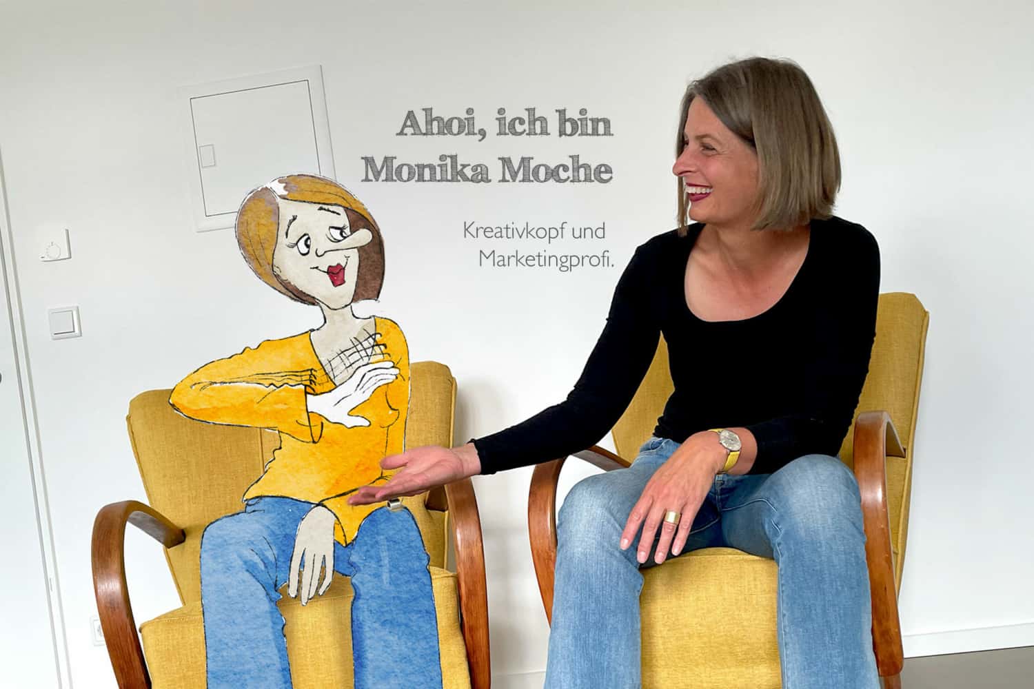 Monika Moche sitzt im Sessel und klatsch ihre gezeichnete Figur ag.